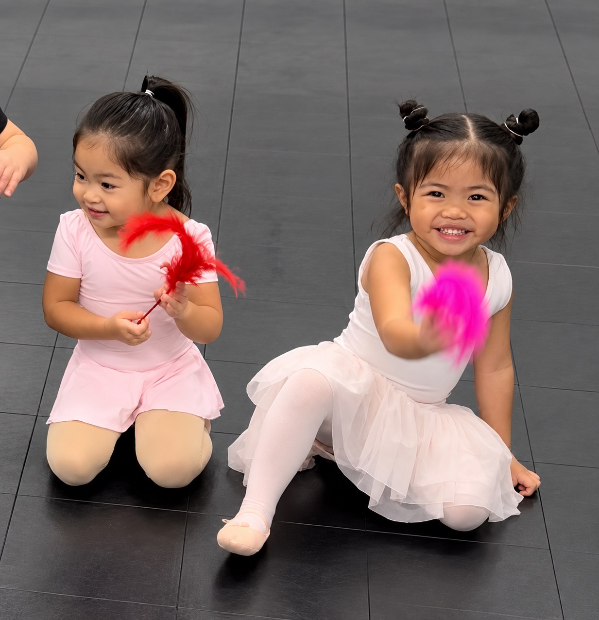Two little girls sitting on the studio floor holding feather wands