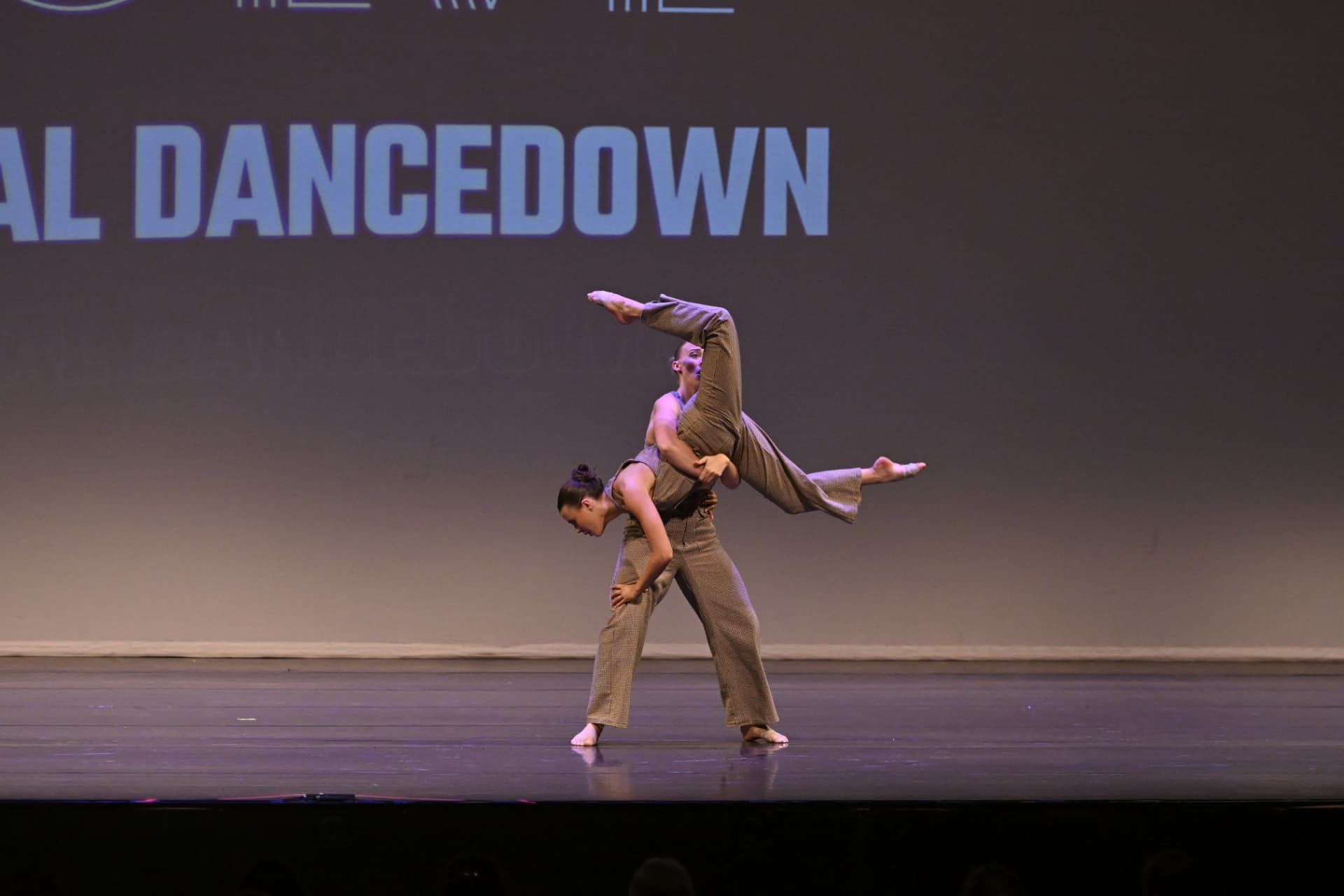 Two Danscott contemporary dancers in brown costumes performing a lift on stage